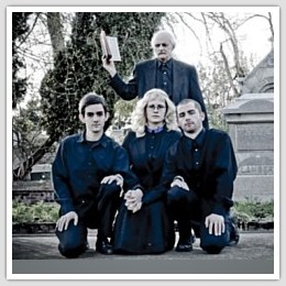 a man holding a bible standing behind three young people in a graveyard